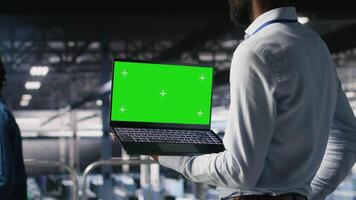Data center programmers on industrial platform using green screen laptop, collaborating on tasks. Server hub workers visualizing large language model architecture using mockup notebook and PC video