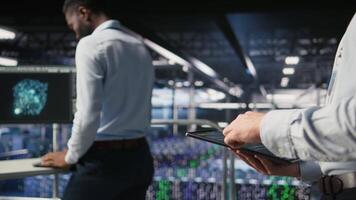 Close up of data center software developer doing maintenance tasks on tablet, ensuring optimal performance. Worker reviewing diagnostics and applying patches to server hub equipment, camera A video