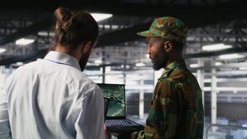 Army operators in data center using laptop to run drone control software, looking at mission map overlay. Military experts doing strategic deployment of autonomous aerial vehicles, camera B video