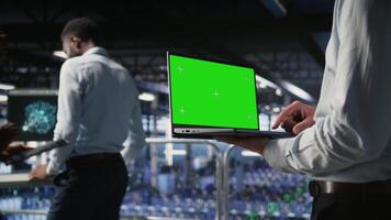 Close up of server room worker using green screen laptop next to colleague reviewing AI LLM visualization. Data center IT professional chroma key notebook to monitor AI systems, camera A video