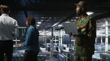 Army information technology specialist in data center troubleshooting military computer systems and networks using laptop. Soldier in command center server room using notebook, camera A video