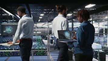 System administrators in data center monitoring AI LLM visualization. African american server farm coworkers overseeing rigs powering machine learning processes, camera A video