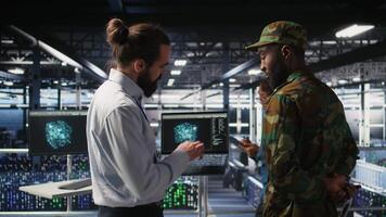 Military personnel overseeing AI computing operations on laptop in high tech server facility. Army tech experts using artificial intelligence to oversee communication systems, camera A video