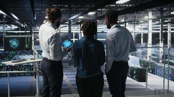 Software developers in data center monitoring AI LLM visualization. Server farm teamworking colleagues doing brainstorming, overseeing rigs powering machine learning processes, camera A video