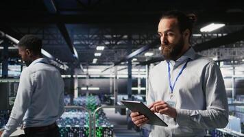 Cheerful data center admin doing maintenance tasks on tablet, ensuring optimal performance. Upbeat IT professional reviewing diagnostics and applying patches to server hub gear, camera A video