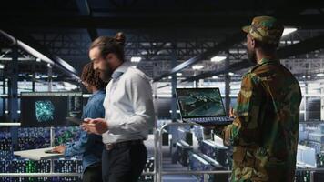 Military technician in data center monitoring warfare drone telemetry on laptop dashboard. IT specialist in army server room using tactical interface on notebook to support aerial operations, camera A video