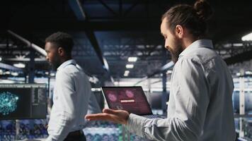 Stressed technicians in server room fighting each other after detecting hacking attempt targeting critical systems. Engineering team members under pressure by virus activity arguing, camera A video
