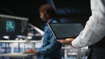 Close up of data center admin using tablet to reviewing machine learning code dashboards. Server farm IT expert using device to monitor AI infrastructure performance, camera A video