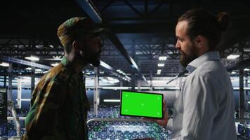 Military technicians in data center use green screen mockup tablet to monitor systems. Army operators in server room ensuring stable infrastructure using chroma key device, camera A video