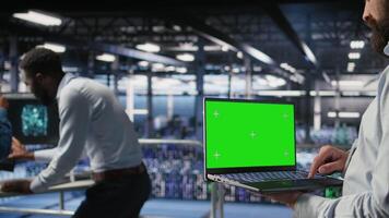 Close up of data center employee doing maintenance tasks on green screen laptop, ensuring optimal performance. Worker using mockup notebook to review diagnostics and apply patches, camera A video