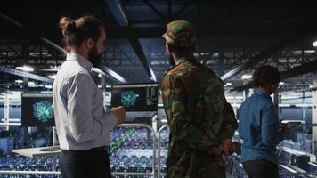 Military server room IT professionals using AI LLM tech on laptop to review network performance. Army operators manage hardware systems supporting mission critical connectivity, camera A video