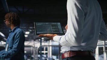 Close up of programmer swiping on tablet display in data center, doing maintenance tasks, ensuring optimal performance. IT expert checks code on device, applying patches to improve stability, camera A video