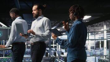 Server hub IT expert monitors systems, doing tech support, guiding users through troubleshooting steps. African american technician providing remote diagnostics using headset mic, camera A video