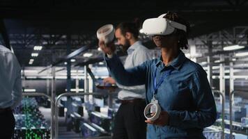 Data center programmer using virtual reality technology to simulate artificial intelligence neural networks. Woman in server farm using VR headset equipment to oversee AI systems, camera A video