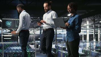 Data center system administrators doing maintenance tasks on laptop, ensuring optimal performance. IT specialists cooperating to review diagnostics and applying patches to server hub gear, camera A video