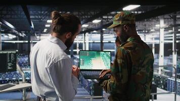Drone operators in military data center supervising autonomous flight systems through laptop interface. Teamworking army IT experts doing live drone tracking using notebook, camera A video
