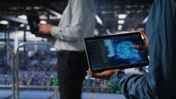 Close up of server farm admin using tablet to do infrastructure AI machine learning automatization. Data center software developer doing maintenance using artificial intelligence, camera A video