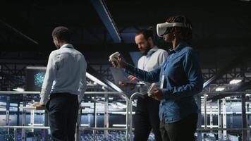 Engineer on data center industrial platform analyzing performance outputs using virtual reality tech. Server hub colleagues finetuning server rig configurations using VR headset tech, camera A video