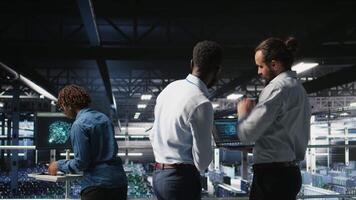 Data center workers cooperating, doing maintenance on rigs handling AI processing tasks. Server hub admins doing brainstorming, managing storage arrays supporting deep learning technology, camera A video