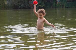 A child plays with a ball in the lake in the summer. People photo