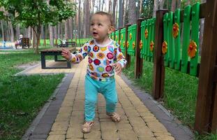 The baby takes his first steps on the playground in the park. People photo