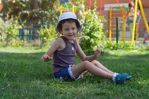 A child in a panama hat sits on the lawn near the playground photo