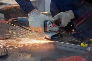 Mechanic using angle grinder and working with metal in workshop. Peoplr photo