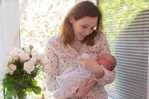 A happy mother with a newborn baby in her arms by the window. photo