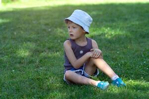 A child in a panama hat sits on the grass in the park photo