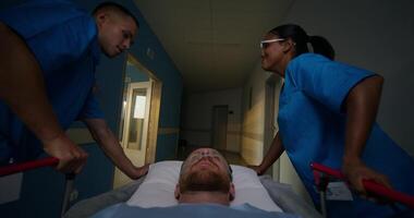 A man with an oxygen tube in his nose is lying on a medical gurney. The orderlies talk and smile photo