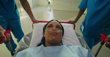 A woman with a breathing tube in her nose is lying on a gurney. She is being driven down the hospital corridor photo