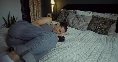 A woman cries when she uses a mobile phone. She's lying on the bed at home photo