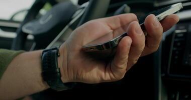 A man connects a mobile phone with a cable to a car while sitting in the driver's seat. Close-up of his hands photo