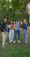 A group of young people with briefcases on their shoulders are smiling at the camera while standing in a city park. photo