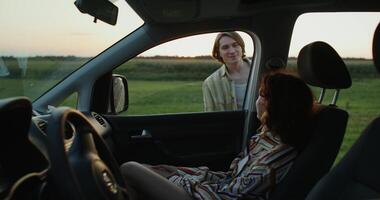 A man and a woman run from a car to a field at sunset. They're holding hands. photo