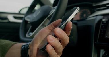 A man connects a mobile phone with a cable to a car while sitting in the driver's seat. Close-up photo