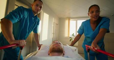 A man with an oxygen tube in his nose is lying on a medical gurney. The orderlies talk and smile as they take the patient through the hospital corridor photo