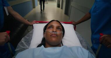 A woman with a breathing tube in her nose is lying on a gurney. She is being driven down the hospital photo