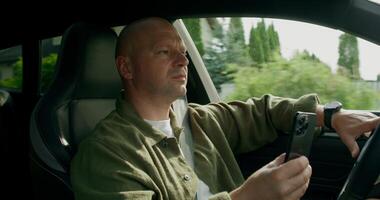 A man taiping on a mobile phone with a serious look while driving a car. View from the car interior. Summer photo