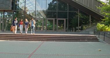 A group of students are talking and smiling as they walk away from the university. Summer day photo