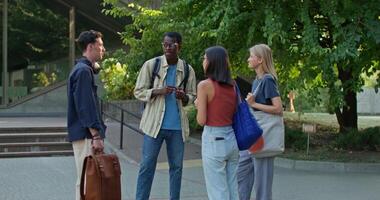 A group of young people with bags and backpacks are talking and smiling standing near the university. Summer day photo
