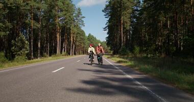 A man and a woman ride bicycles in the middle of a road surrounded by forest. Active leisure on a sunny day photo