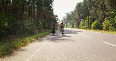 A man and a woman ride bicycles on an asphalt road surrounded by forest. A sunny day photo