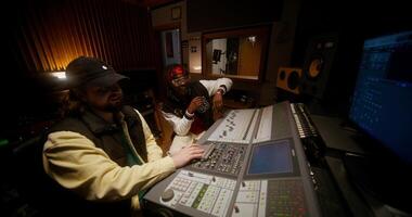 A sound engineer and a singer listen a recorded song sitting in front of an audio mixer. Working in a studio photo