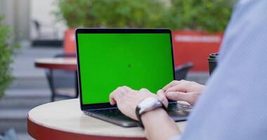 A man typing on a laptop with green screen sitting at a table on a cafe terrace. Close-up of his hands, an unrecognizable person. photo