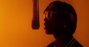 A stylish young man sings into a hanging microphone. Studio in orange light. Close-up of his face photo