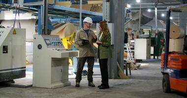 A man and a woman are talking standing in a paper mill. The man holds a tablet in his hand. photo