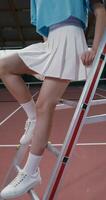 A woman tennis player of Asian appearance in a short skirt sits on the stairs of the referee's chair in the middle of an indoor tennis court and looks at the camera with a serious look, vertical photo