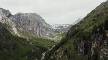 A mountain valley with steep rocky slopes, green hills overgrown with a dense spruce forest, rocky peaks covered with snow and a village in a lowland between the mountains. photo
