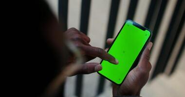 A mobile with a green screen in the hand of a man of African American appearance scrolling the screen, close-up, filming from behind. Copy space, mockup, chroma key. in 4k, red komodo photo
